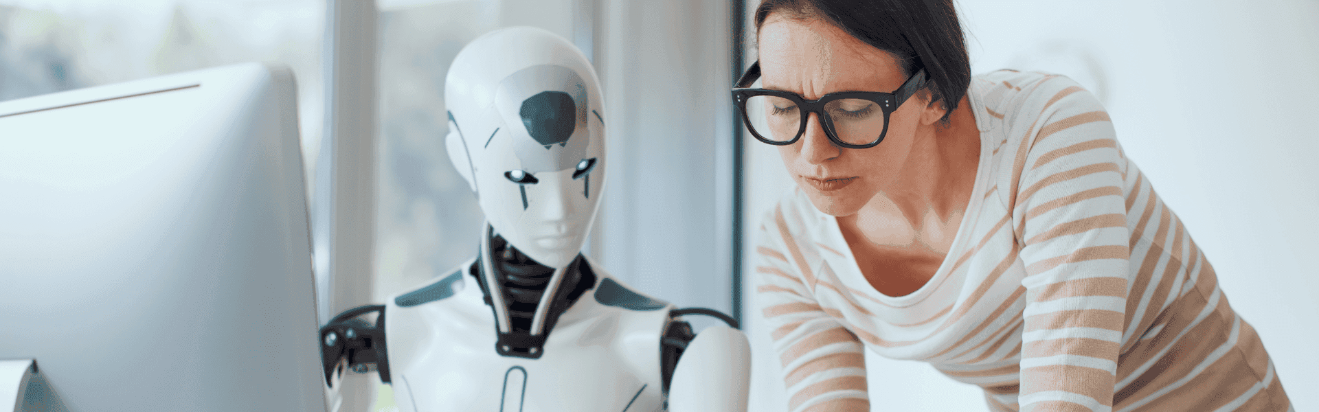 Junge Frau mit Brille spricht mit Roboter am Schreibtisch