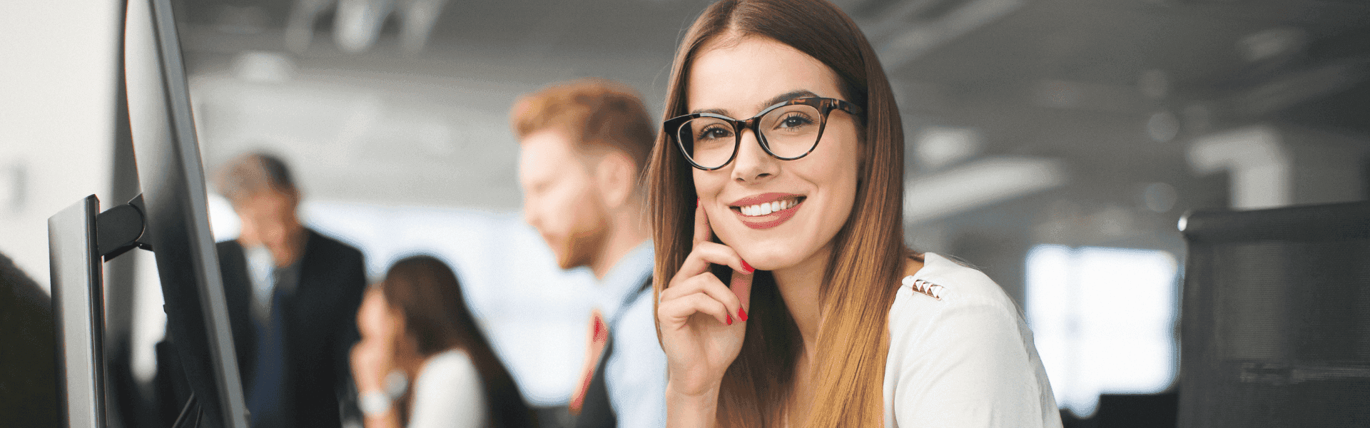 Mitarbeiterin sitzt am Schreibtisch und lächelt in die Kamera